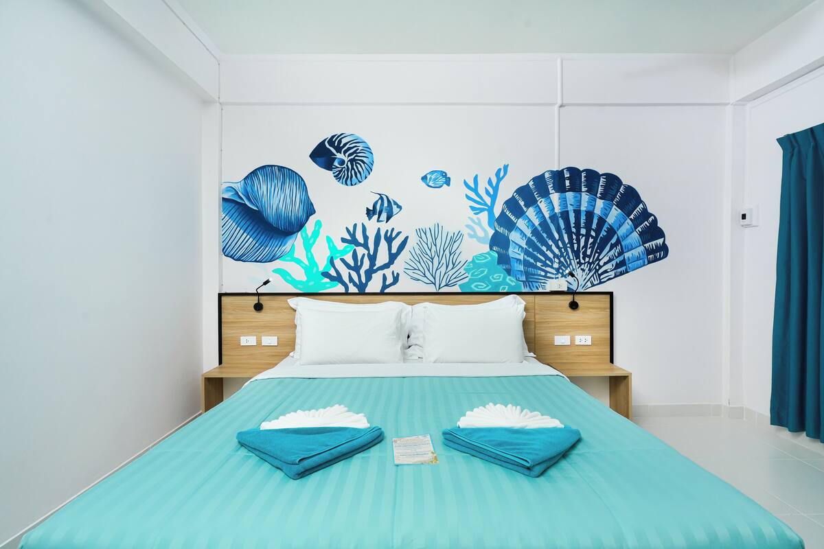 A hotel room with a bed, white pillows, a blue-striped bedspread, and a wall mural of sea life.