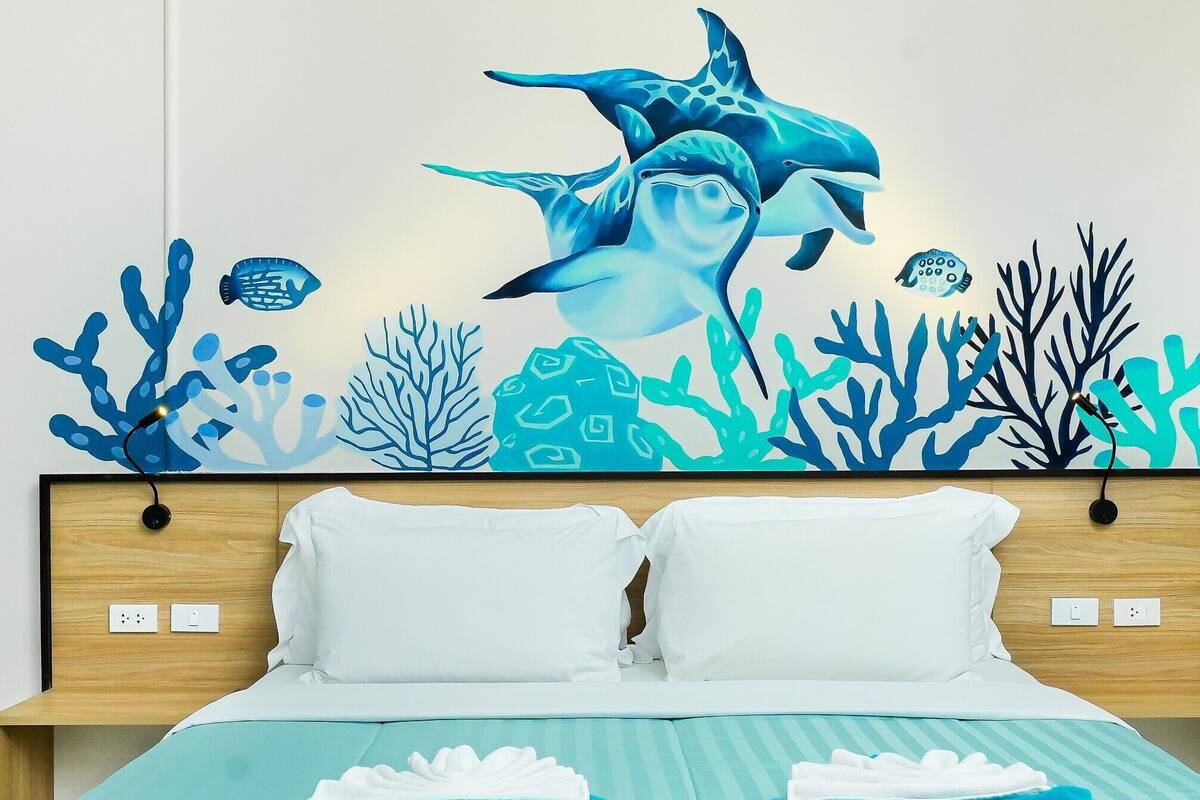 A hotel room with a bed, two pillows, a blue-striped bedspread, and a wall mural of marine life.