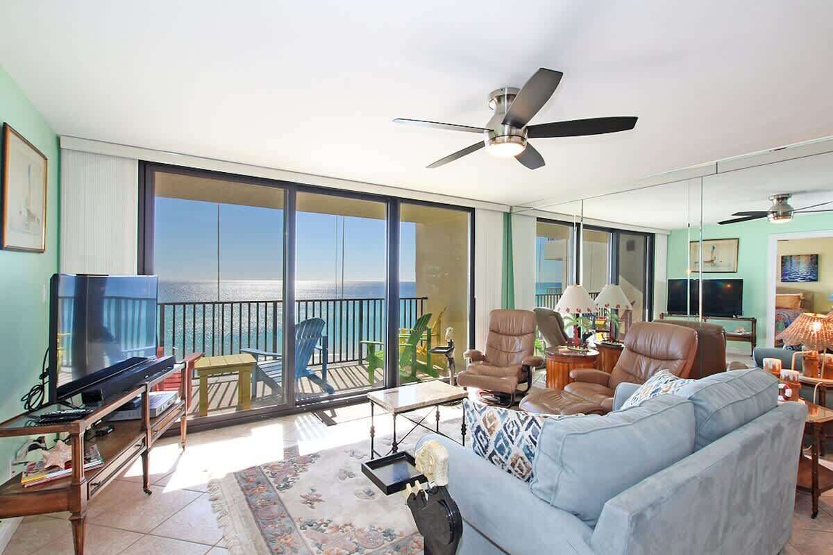 A spacious living room with a large sliding glass door leading to a balcony, a ceiling fan, a sofa, and a television.