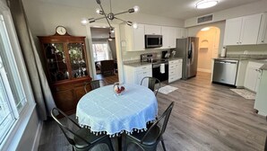 Una cocina moderna con armarios blancos, electrodomésticos de acero inoxidable y un comedor con una mesa redonda y sillas.