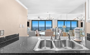A kitchen with a double sink, dining area with wicker furniture, and a view of the ocean through large windows. - 14th-Floor 2BR Condo With Gulf Views, Balcony and Heated Pool Access (Santa Rosa Beach)