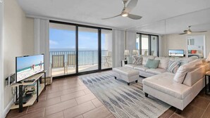 A spacious living room with a large sofa, a flat-screen TV, and a balcony with a view of the beach. - One Seagrove Place 1005 (Santa Rosa Beach)