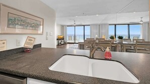 A modern kitchen with a granite countertop, a double sink, and a dining area with a view of the ocean. - One Seagrove Place 1005 (Santa Rosa Beach)