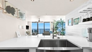 A modern kitchen with a large island, stainless steel appliances, and a view to the outdoors. - One Seagrove Place 1503 (Santa Rosa Beach)