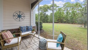 A covered patio with wicker furniture, a compass wall decoration, and a view of a grassy yard with trees. - Golf Getaway at Litchfield by the Sea Beach (Pawleys Island)