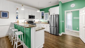 A modern kitchen with white cabinets, a stainless steel refrigerator, and a green accent wall. - Golf Getaway at Litchfield by the Sea Beach (Pawleys Island)