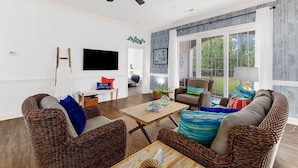 A spacious living room with wicker furniture, a ceiling fan, and large windows offering a view of the outdoors. - Golf Getaway at Litchfield by the Sea Beach (Pawleys Island)