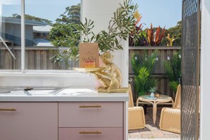 A kitchen with a window, a small dining area with wicker furniture, and a monkey statue. - Palm Springs Villa, Walk to Beaches & Free Parking (Bateau Bay)