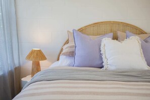 Ein Bett mit gestreifter Bettwäsche, einem gewebten Kopfteil und einer Nachttischlampe.