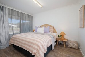 A bedroom with a bed, a nightstand, a lamp, and a window with curtains. - Palm Springs Villa, Walk to Beaches & Free Parking (Bateau Bay)