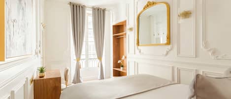 Une chambre d’hôtel avec un grand lit, une commode en bois, un miroir et une fenêtre avec des rideaux.