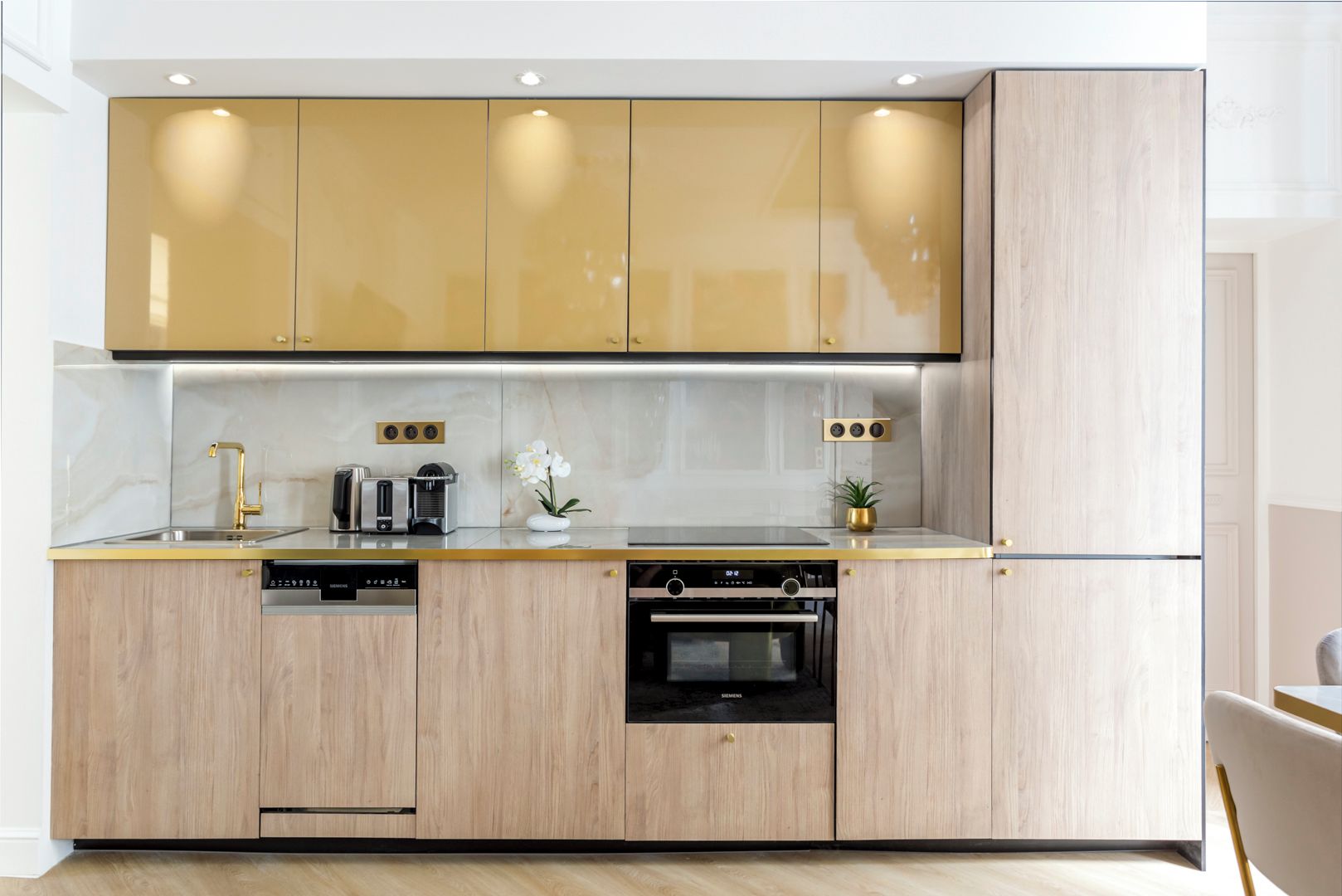 A modern kitchen with wooden cabinets, a stainless steel sink, a built-in oven, and a coffee machine.