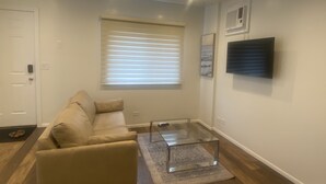 Ett modernt vardagsrum med en soffa, ett soffbord i glas och en tv som är monterad på väggen.