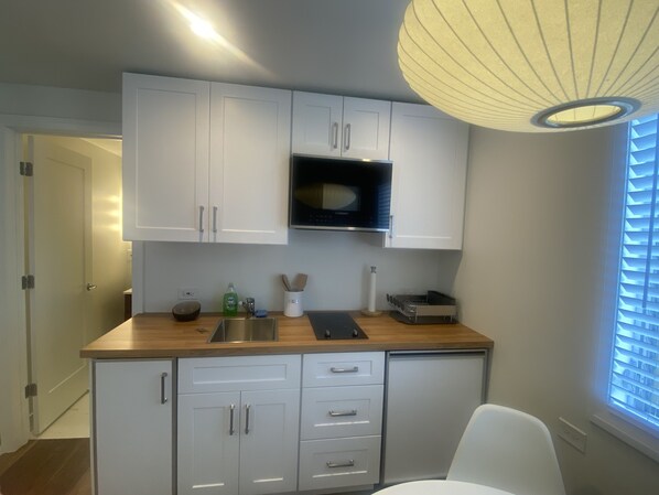 A modern kitchen with white cabinets, a microwave, and a wooden countertop.
