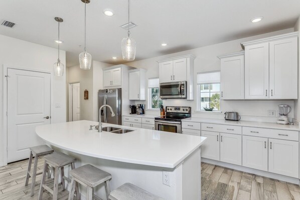 A modern kitchen with white cabinetry, stainless steel appliances, and a large island with stools.