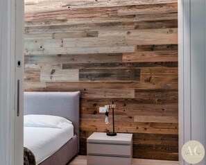 A bedroom with a bed, bedside table, and a nightstand with a lamp.