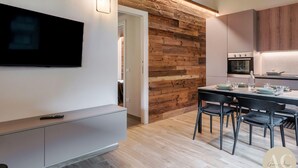 Una cocina moderna con una pared de acento de madera, un comedor con mesa y sillas, y un televisor montado en la pared.