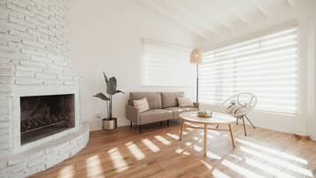 A living room with a white brick fireplace, a beige sofa, a round wooden coffee table, and a white chair.