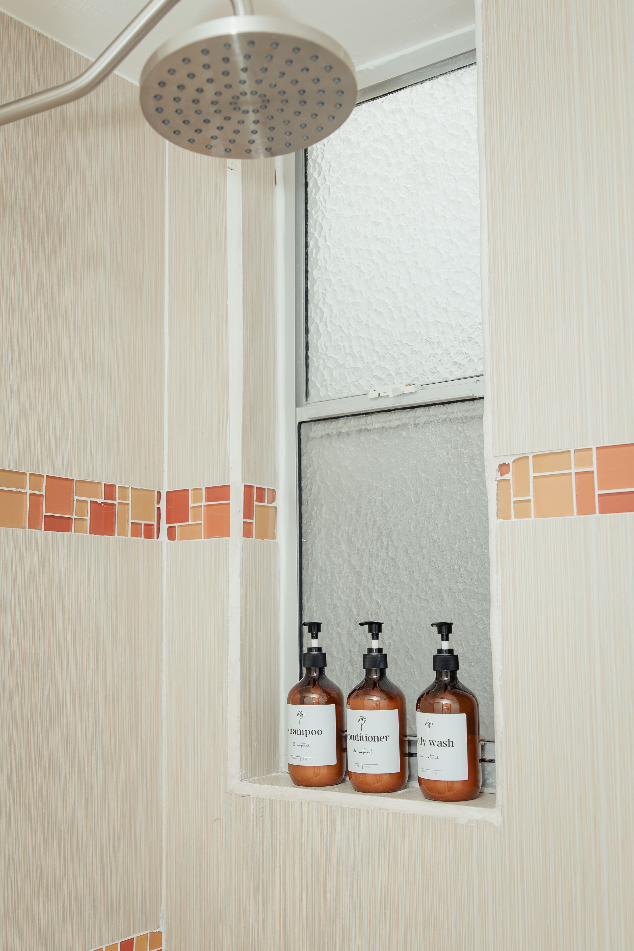 Une salle de bain avec une douche, une fenêtre et trois bouteilles de shampoing, d’après-shampoing et de gel douche.