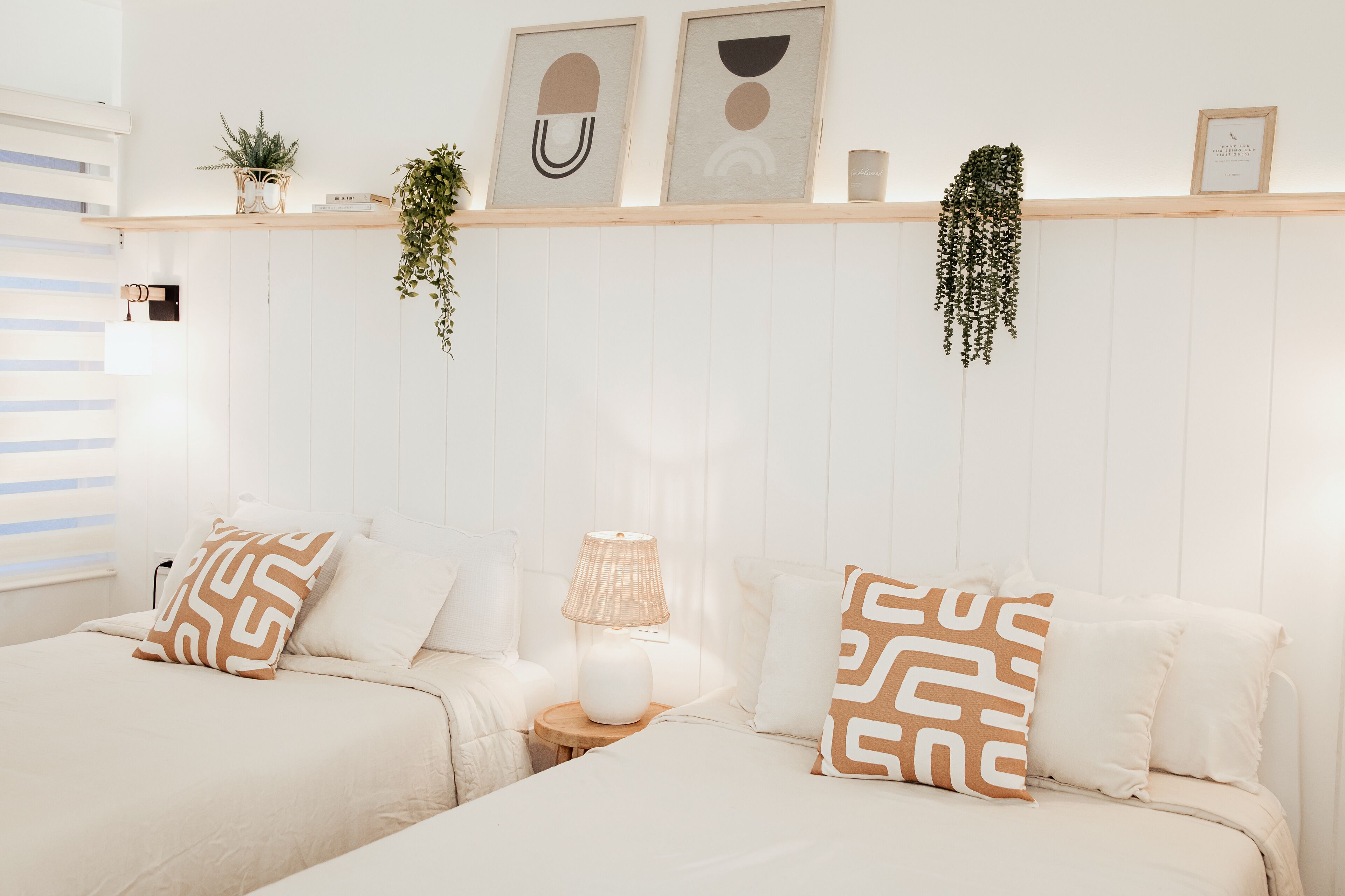 Una camera da letto con due letti, un comodino con una lampada e una mensola a parete con oggetti decorativi.