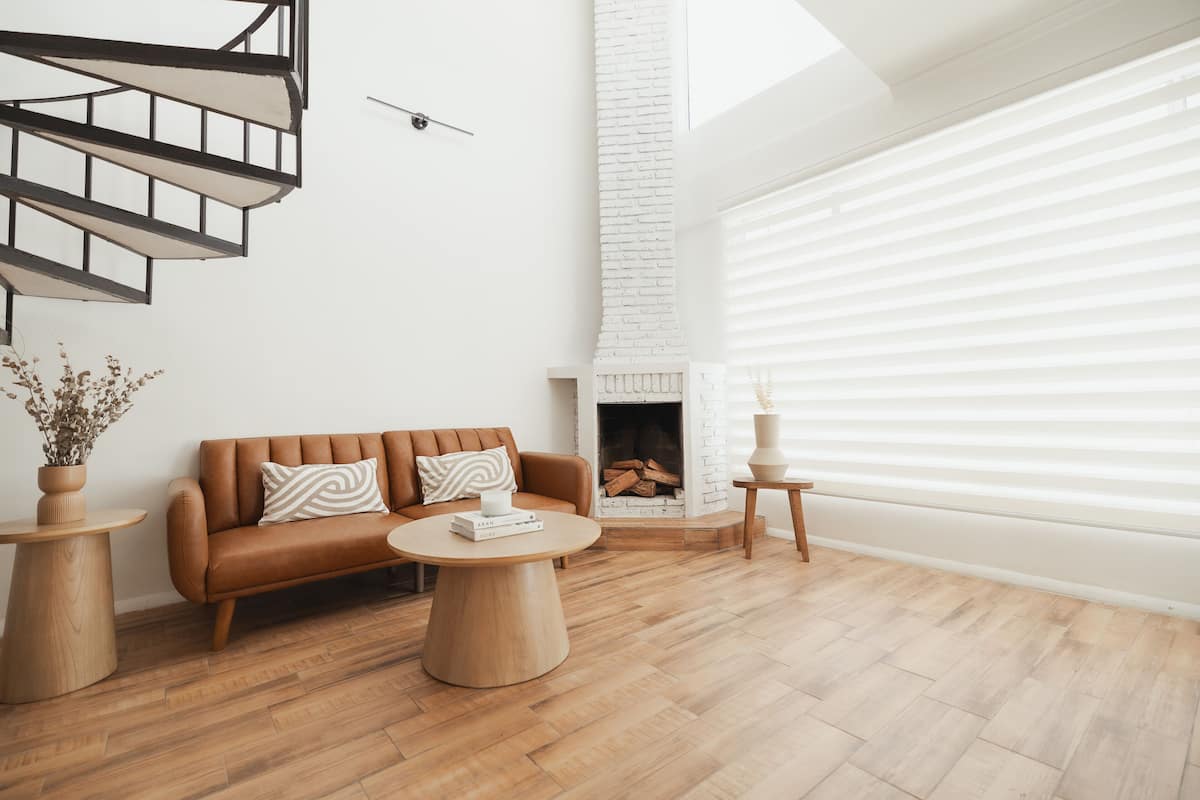 A modern living room with a brown leather sofa, a round wooden coffee table, and a white brick fireplace.