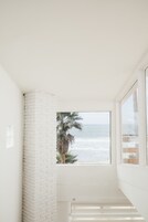 A room with a white brick wall, a large window with a view of the ocean, and a staircase.