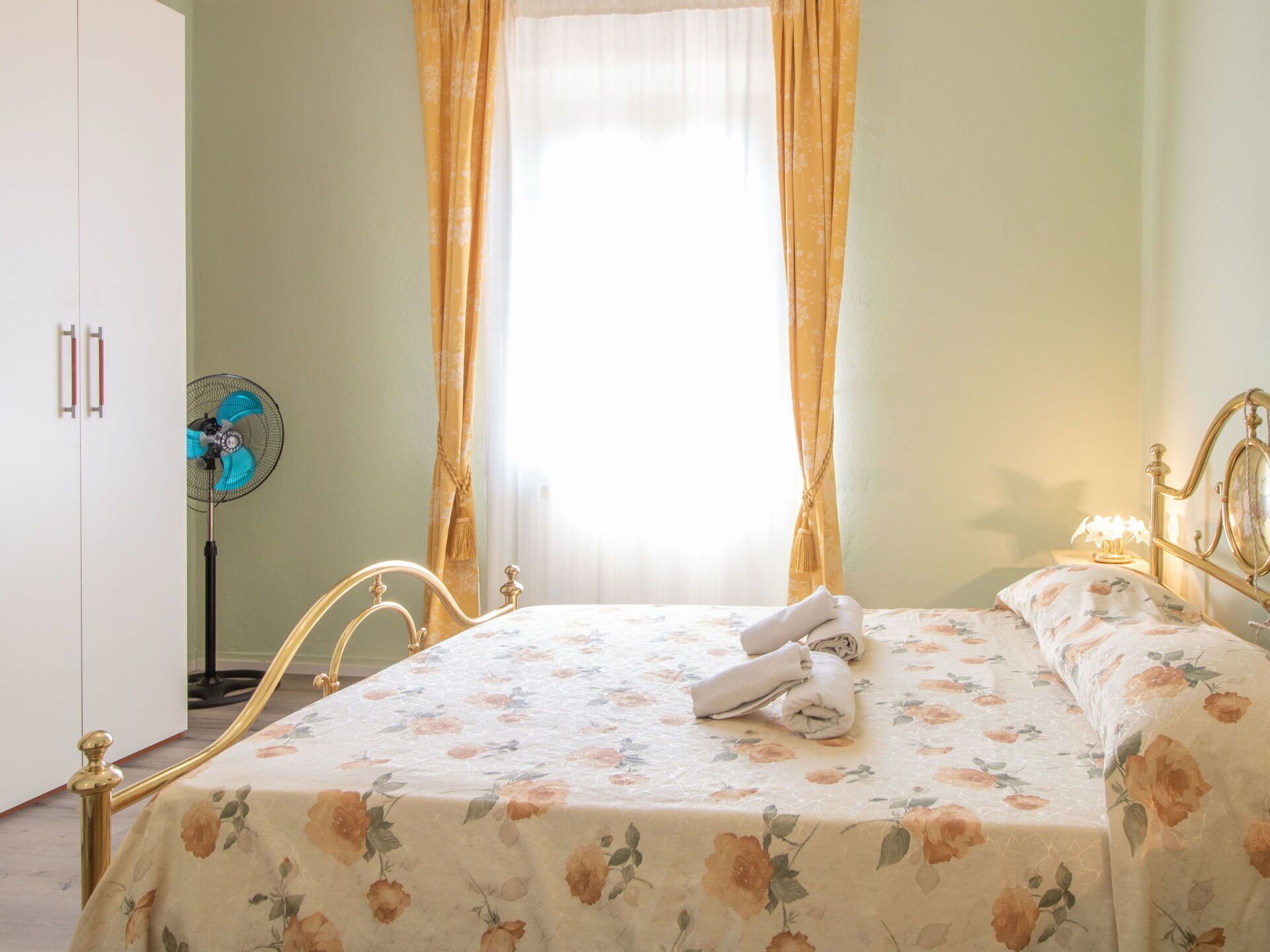 Ein Schlafzimmer mit einem Bett, Vorhängen, einem Ventilator und einem Nachttisch mit einer Lampe.