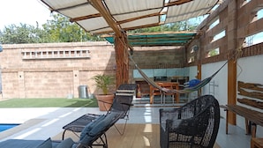 A covered patio area with lounge chairs, a pool, and a dining table.