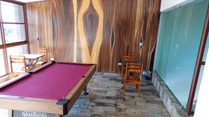 A billiards room with a pool table, wooden chairs, and a herringbone-patterned floor.