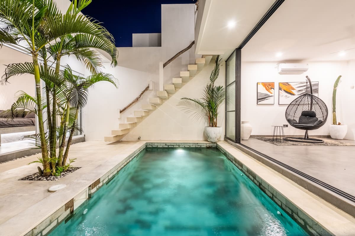 A modern outdoor pool area with a staircase leading to a covered upper level, surrounded by potted plants and minimalist furniture.