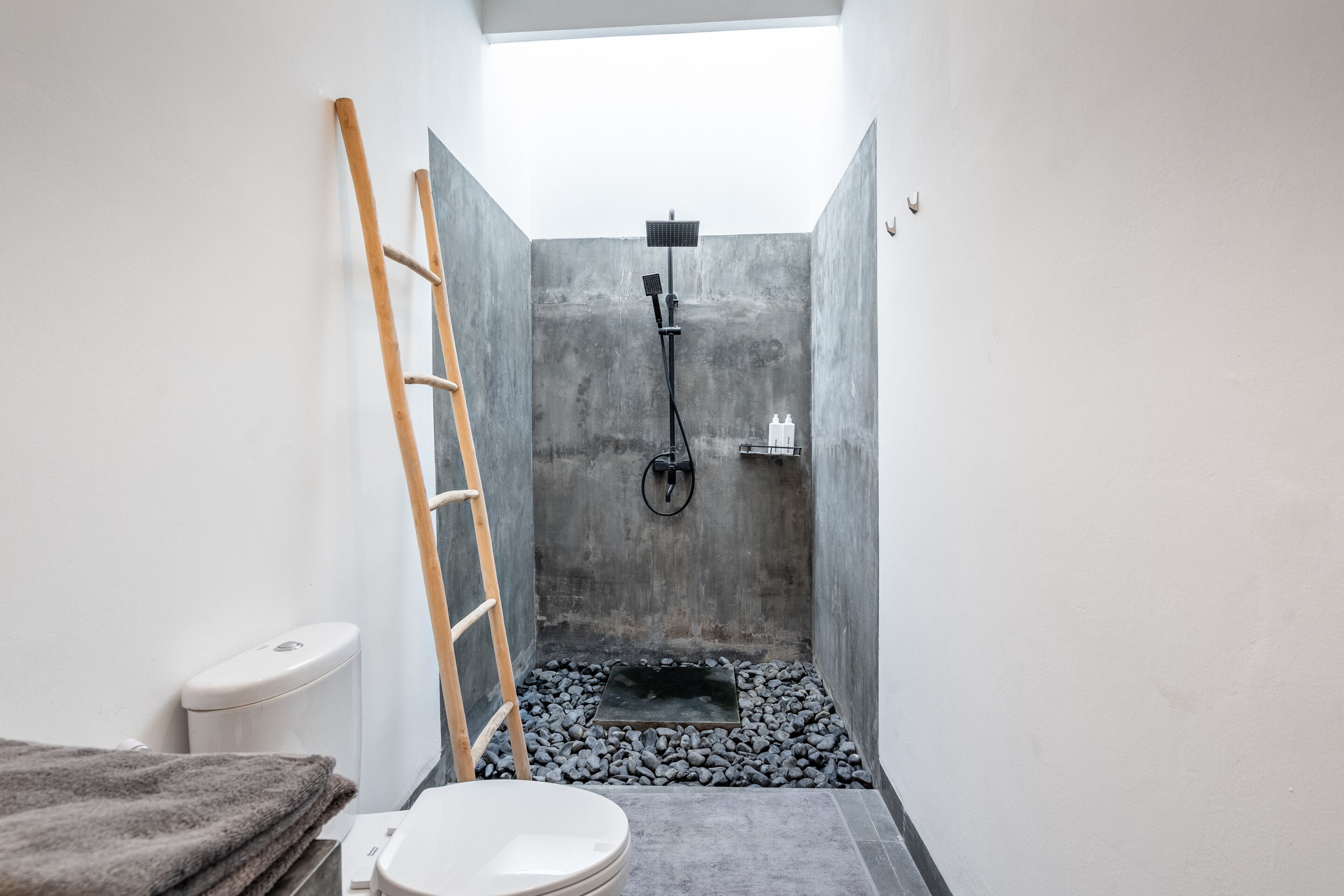 A narrow bathroom with a shower, toilet, and a wooden ladder.