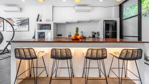 A modern kitchen with a wooden countertop, three black bar stools, and pendant lighting. - Sunny Home Villa (Canggu)
