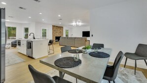 A modern kitchen with a central island, a dining area with a table and chairs, and a living area with a sofa and TV. - Quiet 3BR Near Hospital & Georgia Southern | 2 King Beds + Workspace (Statesboro)