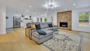 A modern living room with a grey sectional sofa, a fireplace, and a kitchen in the background. - Quiet 3BR Near Hospital & Georgia Southern | 2 King Beds + Workspace (Statesboro)