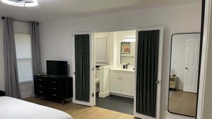 A bedroom with a bed, a TV on a dresser, and a bathroom with a sink and toilet visible through an open door. - Quiet 3BR Near Hospital & Georgia Southern | 2 King Beds + Workspace (Statesboro)