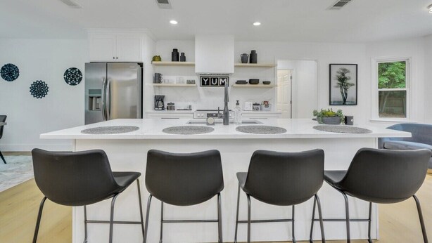 A modern kitchen with a central island, black bar stools, and a stainless steel refrigerator. - Quiet 3BR Near Hospital & Georgia Southern | 2 King Beds + Workspace (Statesboro)