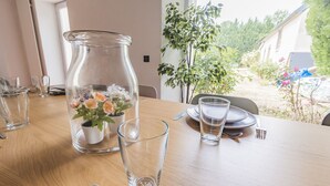 Ein Esstisch gedeckt mit klarem Glas, einer Blumenvase und Blick auf einen Garten.
