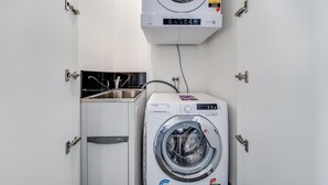 A compact laundry room with a front-loading washing machine, a sink, and a wall-mounted dryer. - Chic 1-Bed with Stunning Lake View & Indoor Pool (Belconnen)