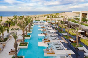 Een resort met een centraal gelegen zwembad, ligbedden en uitzicht op het strand.