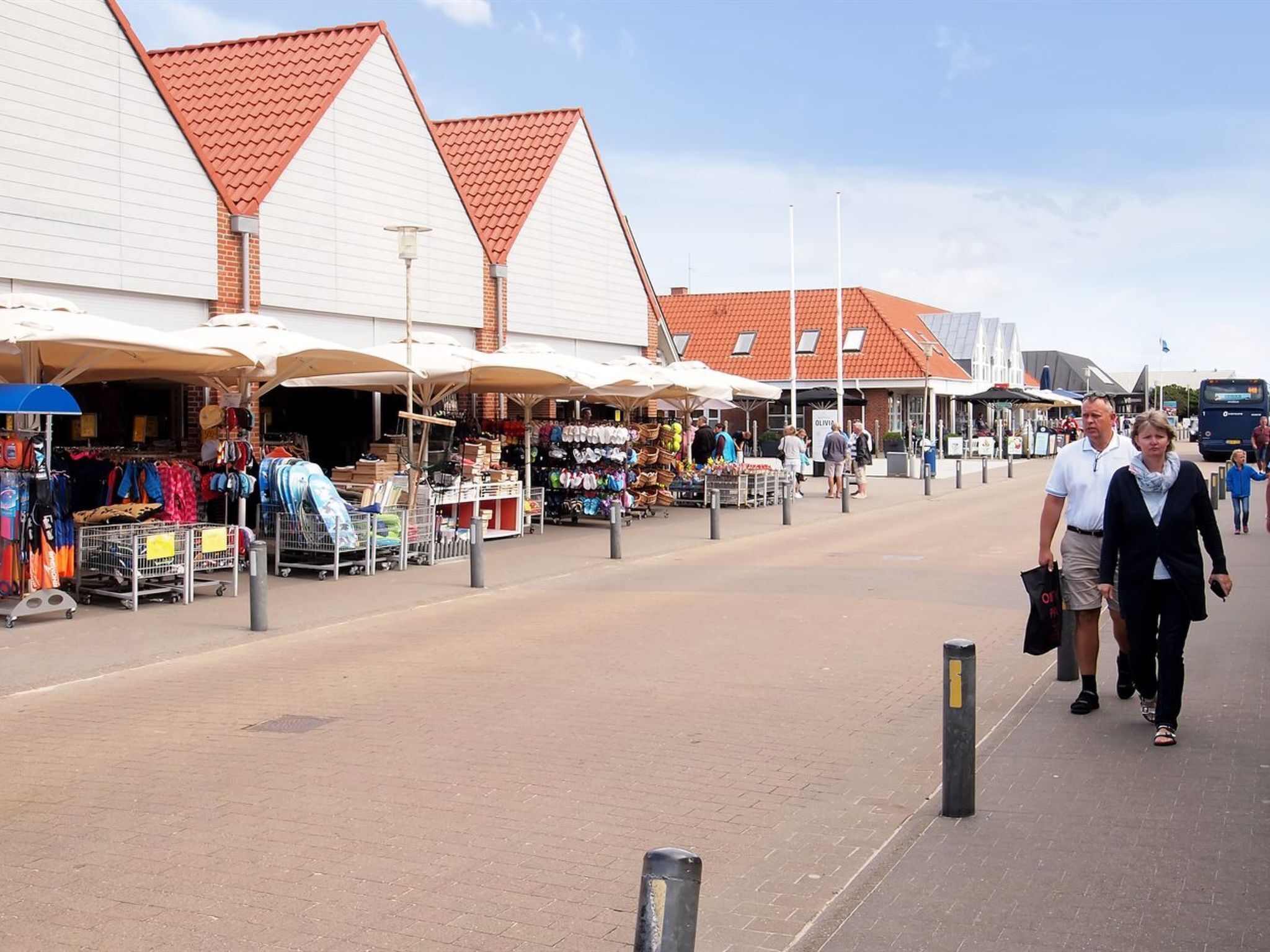 A pedestrian walkway with outdoor market stalls and a building with a red-tiled roof.