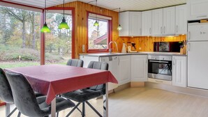 Een moderne keuken met witte kasten, een roestvrijstalen oven en een eethoek met een rode tafelkleed en grijze stoelen.