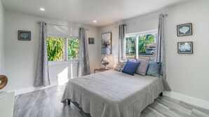 A bedroom with a bed, curtains, a nightstand, and a window with a view of greenery.