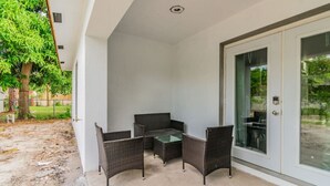 A covered patio area with a table and chairs, a sliding glass door, and a view of a tree and yard.