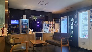 Interior moderno de una cafetería con asientos, una máquina de café, un refrigerador y una máquina expendedora.