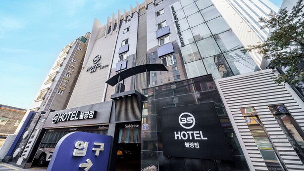 Un moderno edificio hotelero con varios pisos, una entrada destacada y señalización que dice 'HOTEL' y 'Noblesse'.