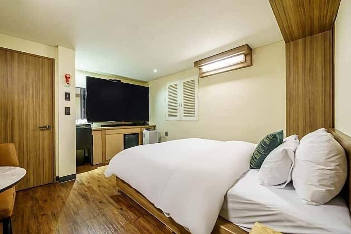 Ein Hotelzimmer mit Bett, einem kleinen Tisch, einer Küchenzeile und einem Fernseher.