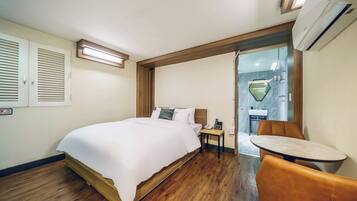 Een hotelkamer met een bed, nachtkastje, stoel en een klein tafeltje met een stoel.