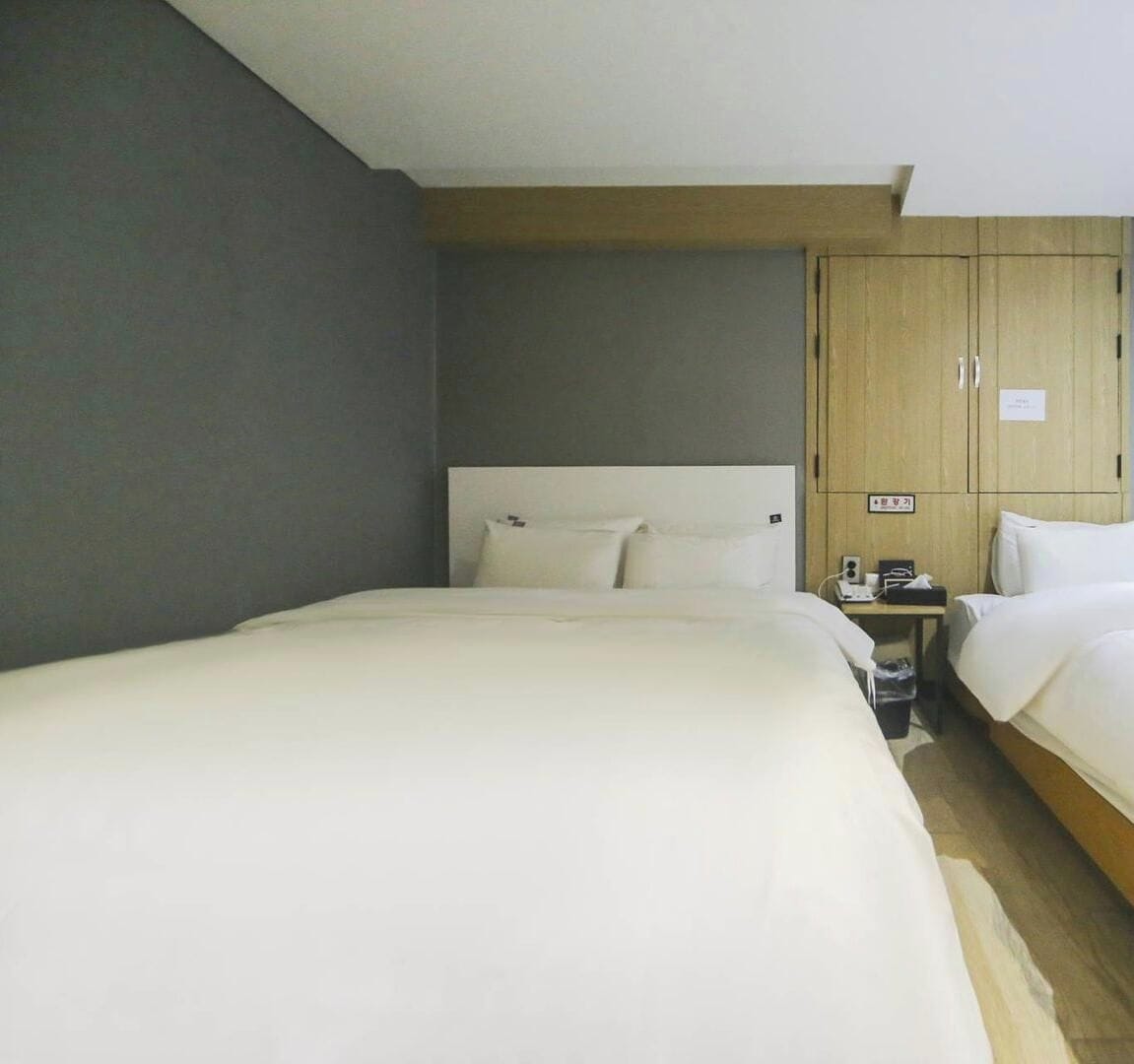 A hotel room with two beds, a wooden wardrobe, and a small bedside table with a lamp.