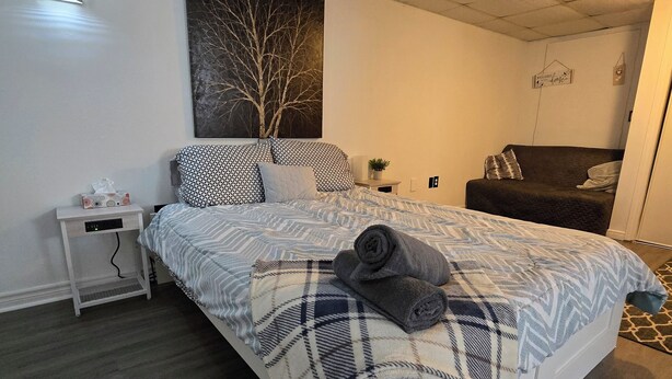 A neatly arranged bedroom with a bed, bedside table, and a sofa. - Spacious, Pet Friendly Basement Apartment  (Milton)