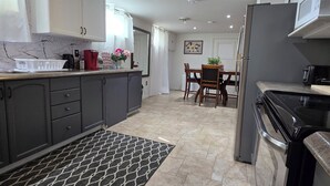 A modern kitchen with grey cabinets, a black and white patterned rug, a dining area with a table and chairs, and a refrigerator. - Spacious, Pet Friendly Basement Apartment  (Milton)